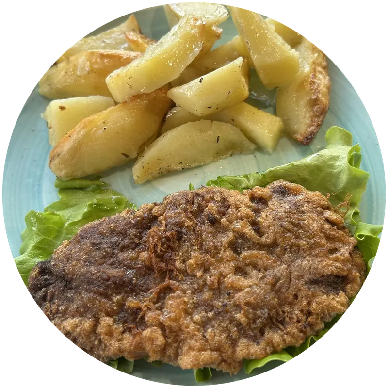 Breaded Viennese cutlet on lettuce with oven potatoes, on a pale blue plate
