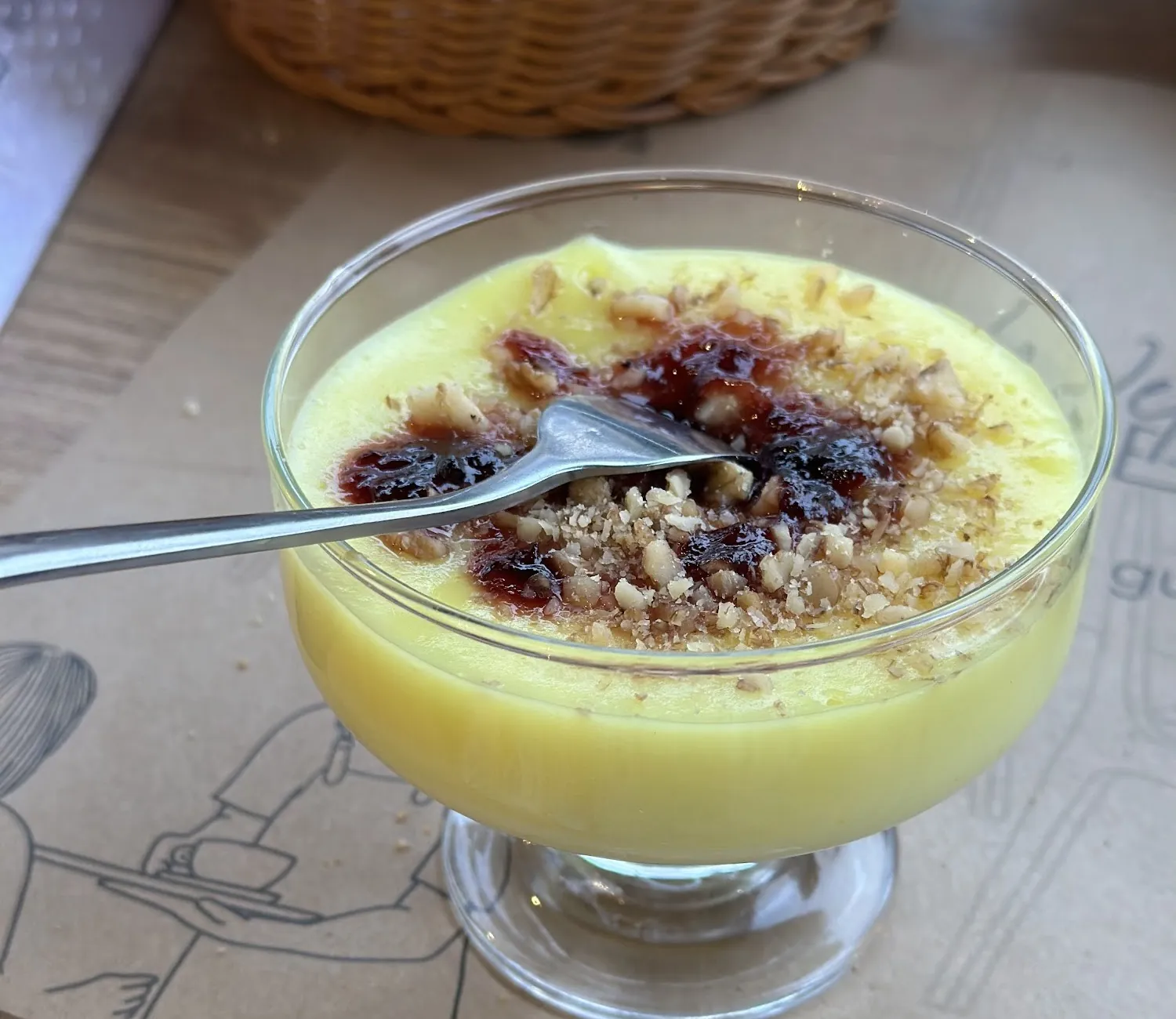 A glass of custard topped with jam and crushed walnuts on a Rustemi placemat