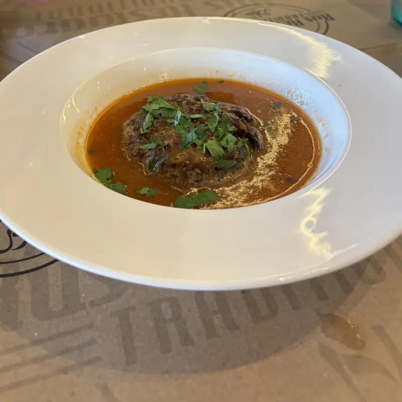 Meat in a red broth with fresh parsley, in a wide white bowl