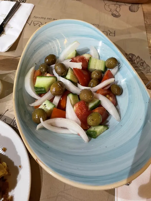 Village salad with olives, tomato, cucumber and onion on a blue plate